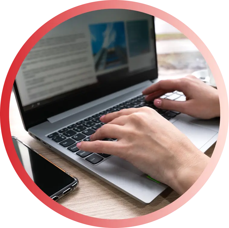 Hands typing on a silver laptop keyboard with a smartphone beside it on a wooden desk